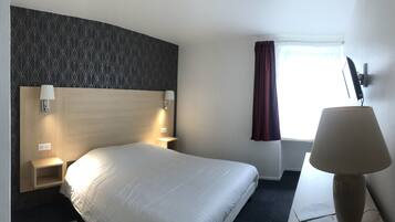 Habitación de hotel con una cama grande, cabecera con diseño geométrico, lámparas de noche, escritorio, silla, ventana con cortinas y televisión montada en la pared.