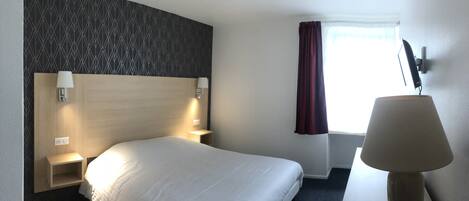 Habitación de hotel con una cama grande, cabecera con diseño geométrico, lámparas de noche, escritorio, silla, ventana con cortinas y televisión montada en la pared.
