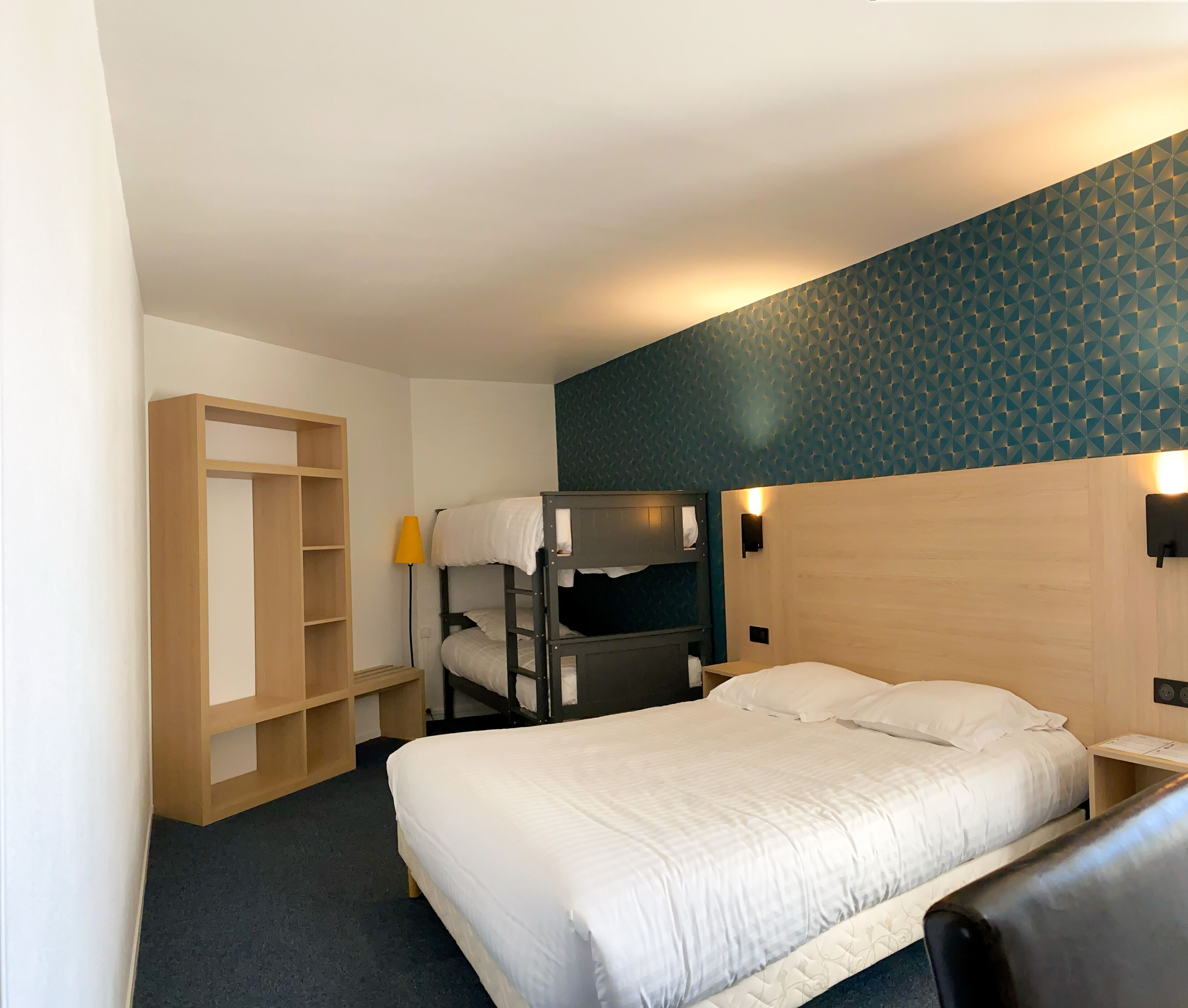 Une chambre d’hôtel avec un lit superposé, une armoire en bois, un bureau avec une lampe et un mur décoré de motifs.