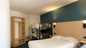 Une chambre d’hôtel avec un lit superposé, une armoire en bois, un bureau avec une lampe et un mur décoré de motifs.
