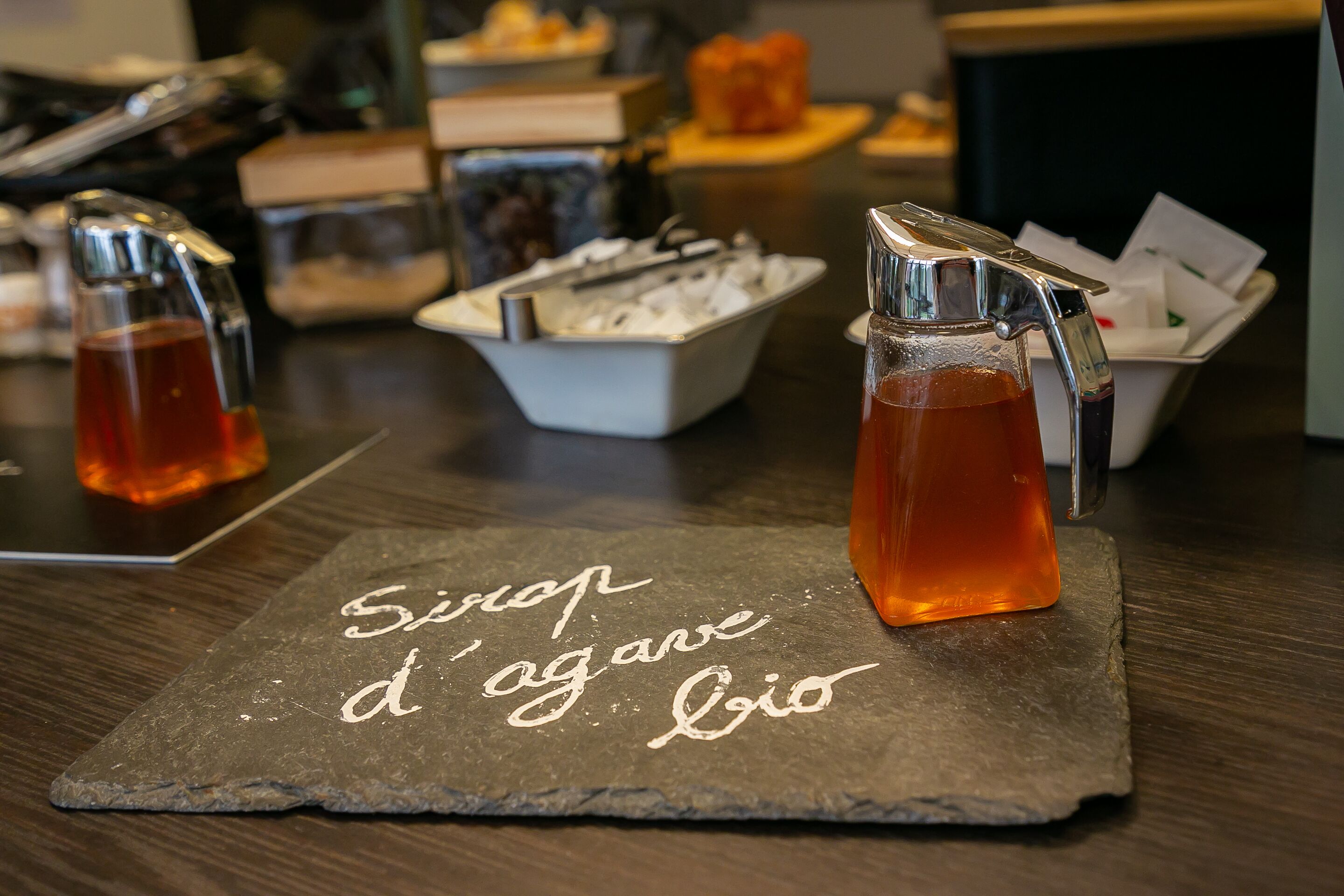 A slate serving tray with a beverage dispenser and a bowl of ice cubes on a wooden table.