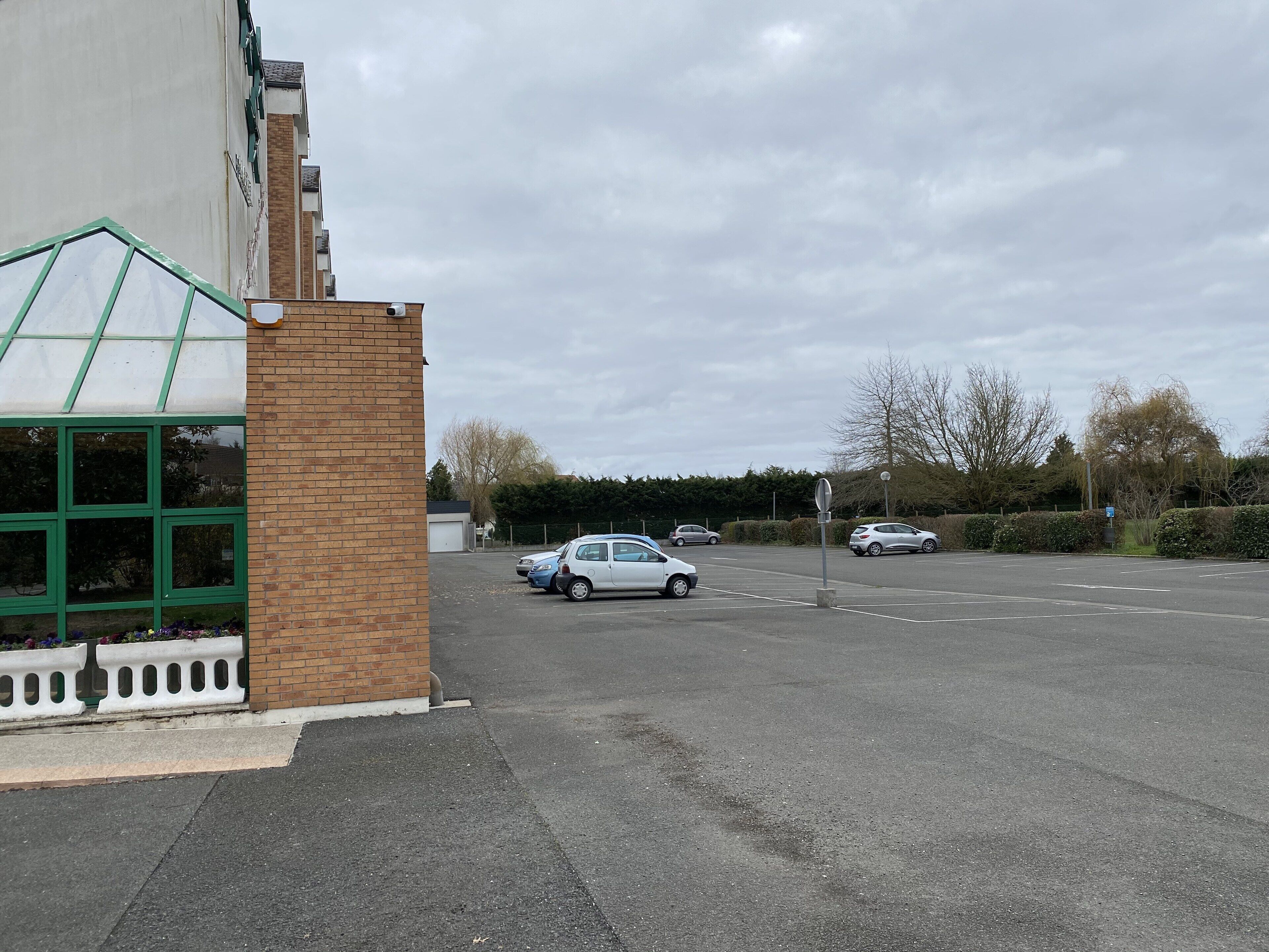 A parking lot with cars, a building with a green window frame, and a brick wall.