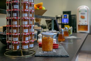 A display of jars with labels, a bowl of fruit, and a coffee machine on a counter. - Cit' Hôtel la Pyramide (Romorantin-Lanthenay)
