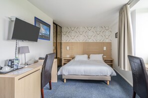 A hotel room with a bed, desk, chair, TV, and a window with curtains. - Cit' Hôtel la Pyramide (Romorantin-Lanthenay)