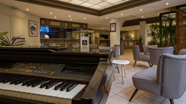 A piano in a lobby with a bar and seating area. - Cit' Hôtel la Pyramide (Romorantin-Lanthenay)