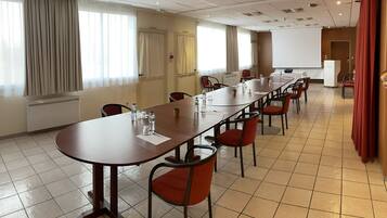 Un salón de conferencias con una larga mesa, sillas rojas y una pantalla para proyector.