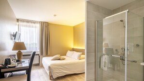 A hotel room with a bed, desk, chair, and a glass-enclosed shower area. - Cit' Hôtel la Pyramide (Romorantin-Lanthenay)
