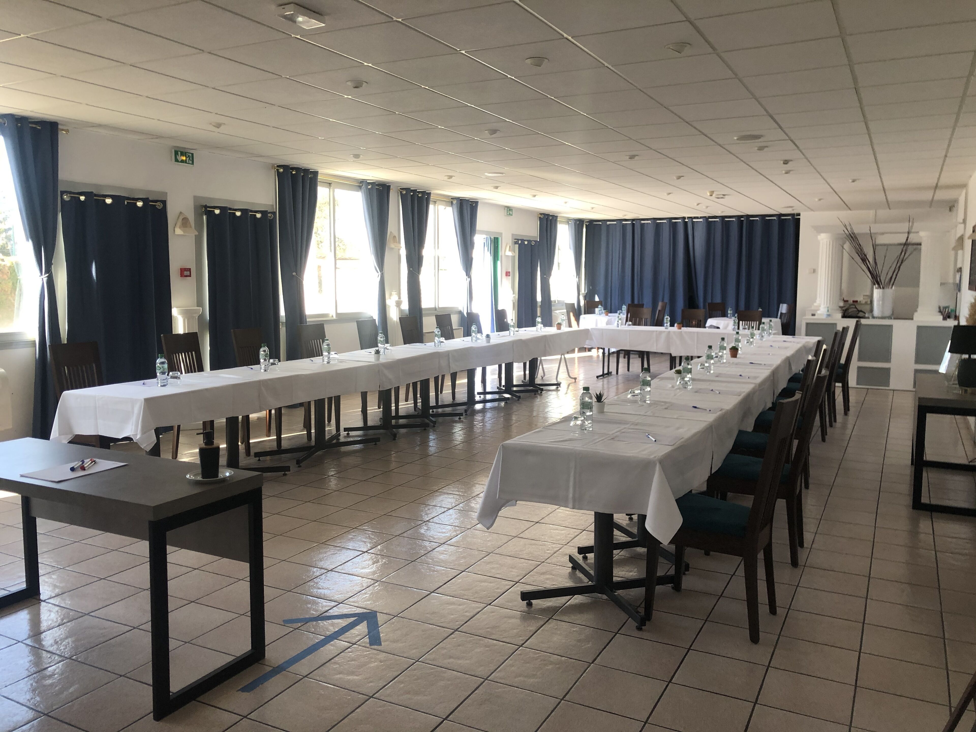 Una sala conferenze con lunghe tavolate, sedie e pavimento piastrellato.