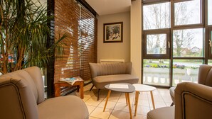 A modern interior with a sofa, two chairs, a small table, and a large window offering a view of the outdoors. - Cit' Hôtel la Pyramide (Romorantin-Lanthenay)