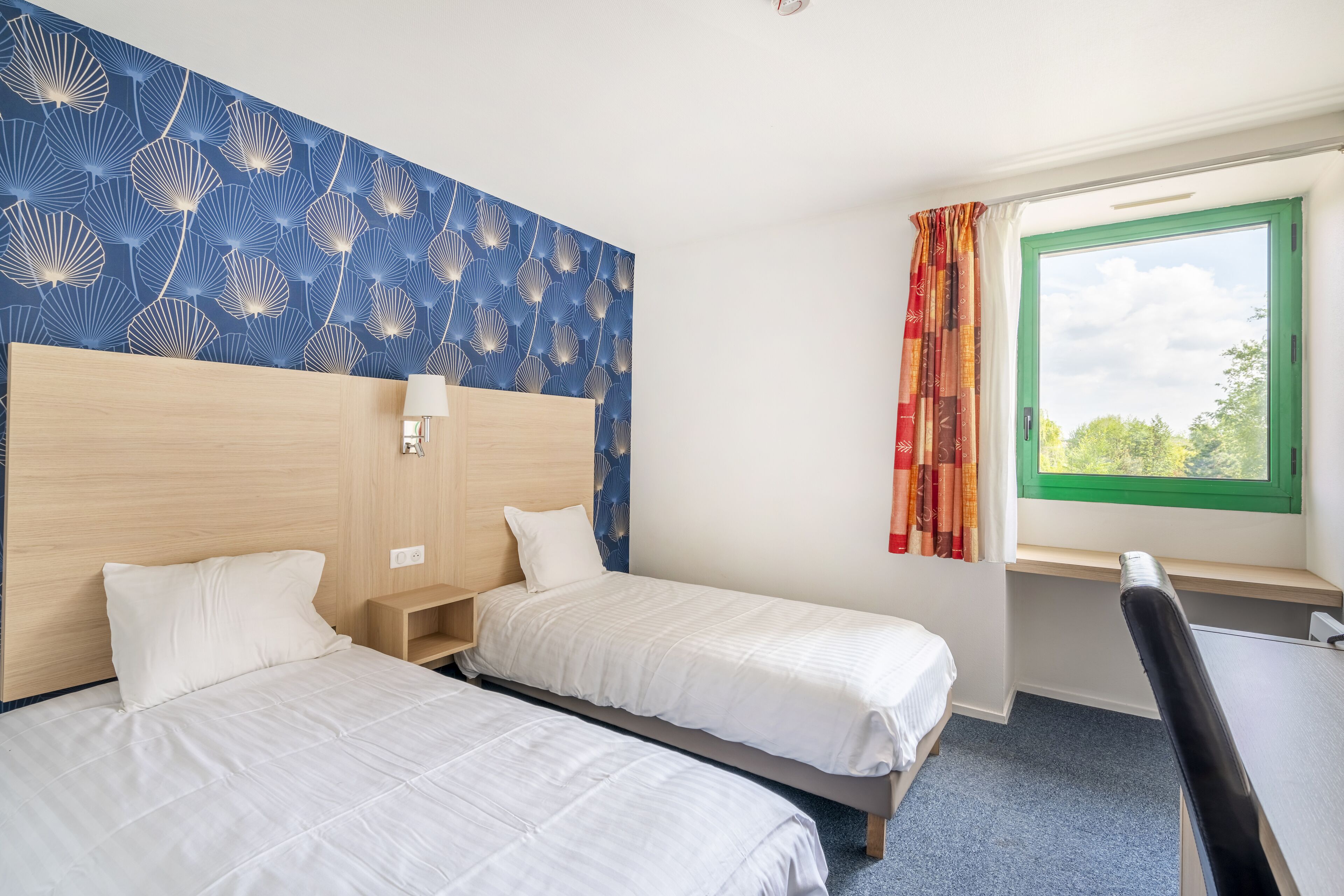 Quarto de hotel com duas camas, uma mesa e uma janela com cortinas.