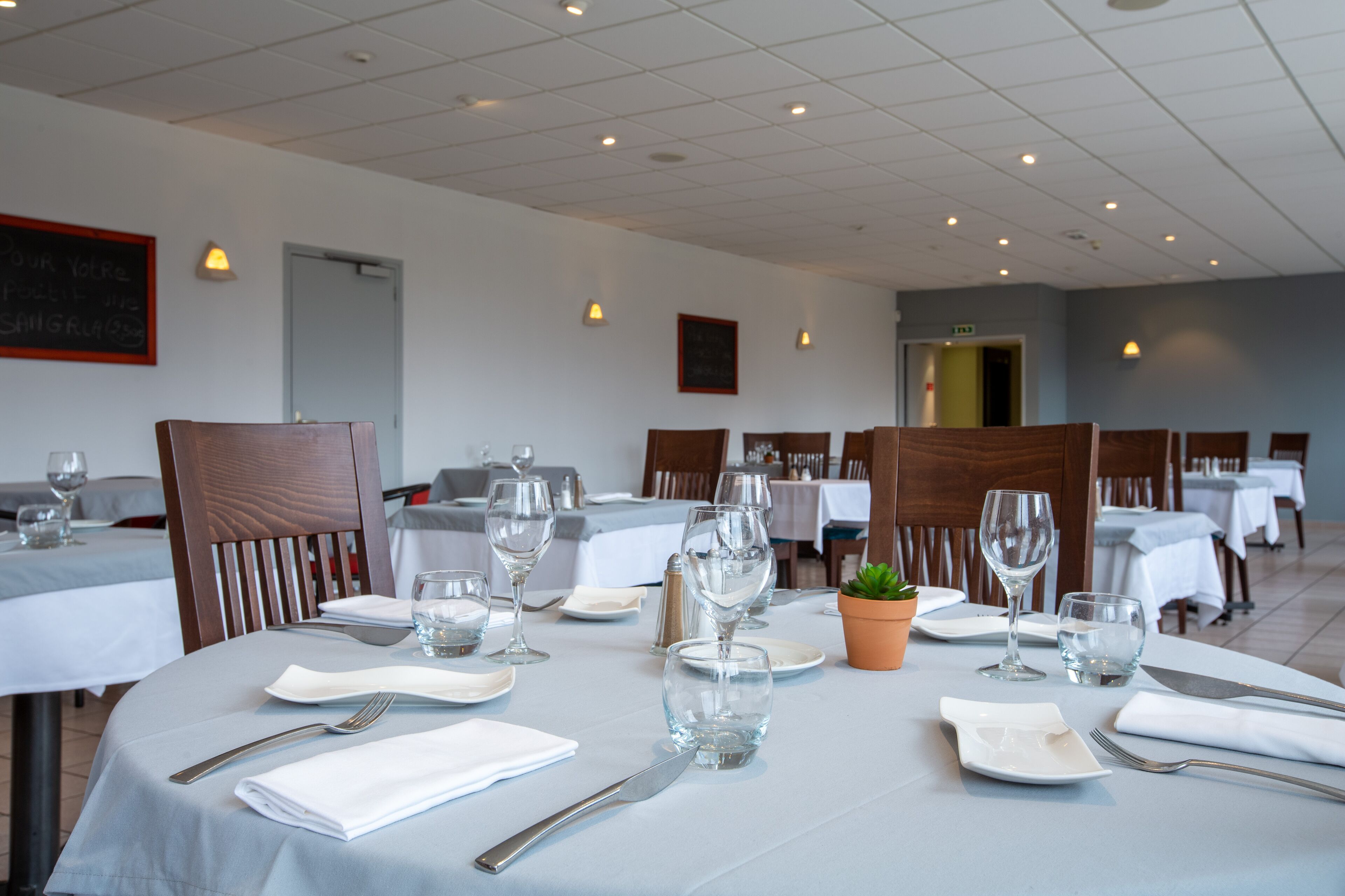 A dining area with tables set for two, each with cutlery, plates, and glasses.