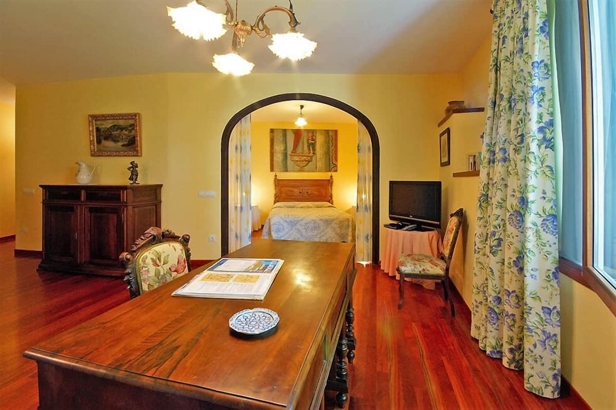 Habitació d'hotel amb taula de dinar de fusta, llit amb capçalera, televisió i escriptori amb cadira.