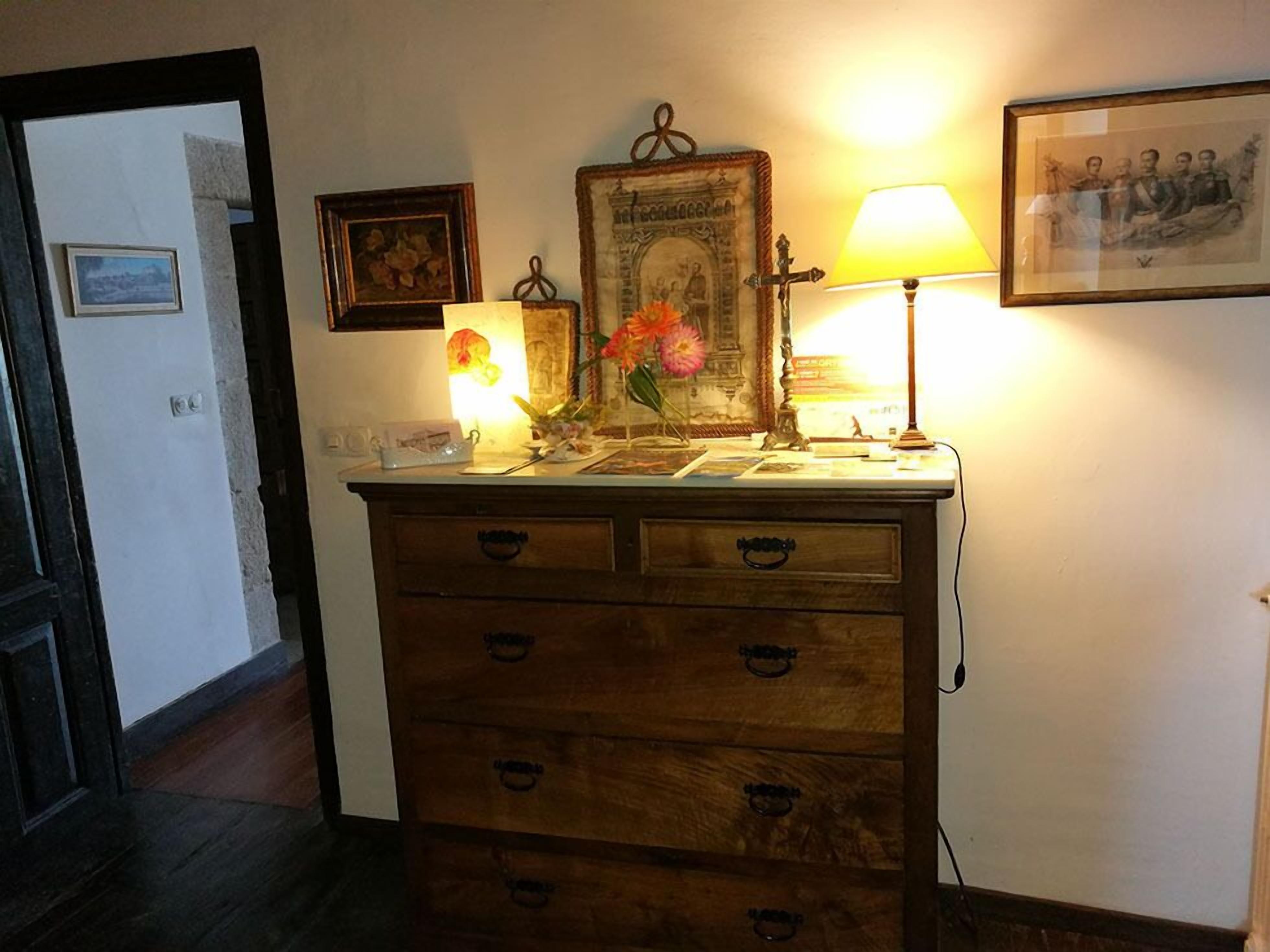 Un aparador de madera con cajones, un cuadro enmarco, una lámpara y un florero con flores.