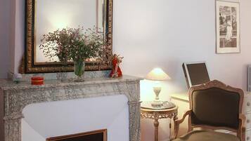 Une pièce avec une cheminée, un grand miroir décoratif, une petite table avec une lampe, une chaise et un tableau encadré au mur.