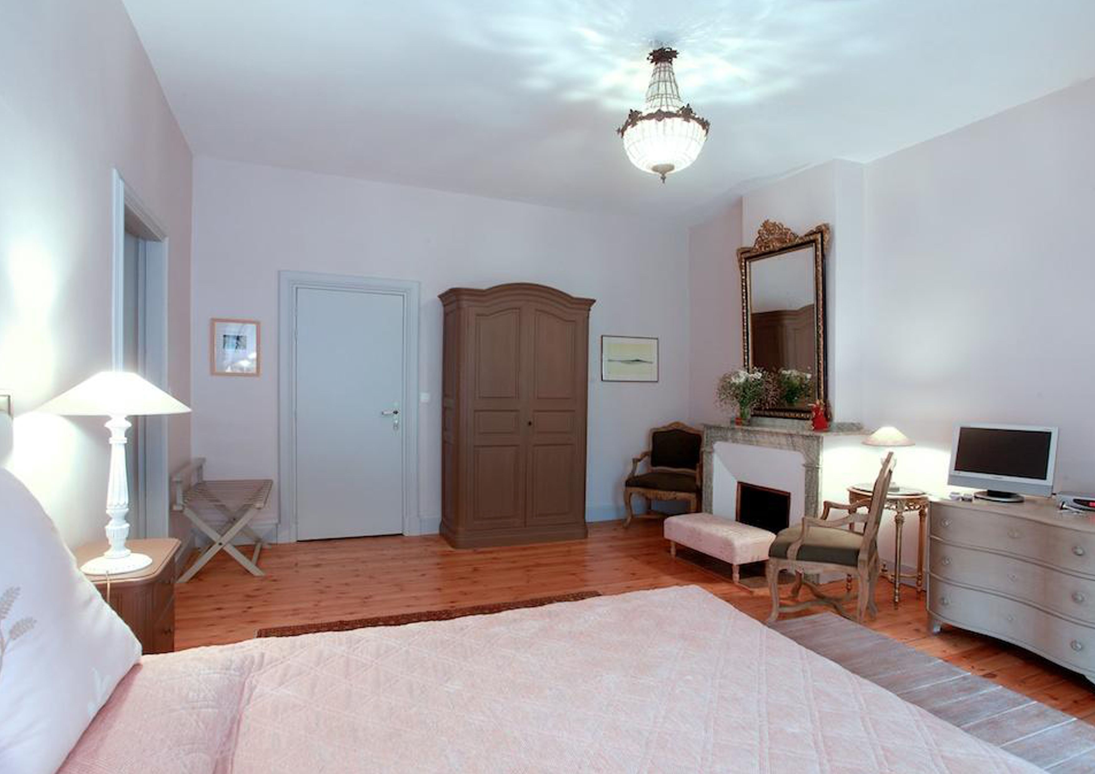 A bedroom with a bed, a wardrobe, a desk with a computer, a chair, a fireplace, and a mirror.