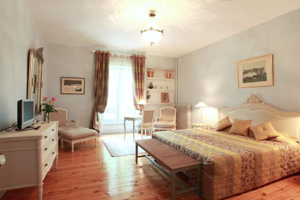 A bedroom with a bed, a desk, a chair, a dresser, and a window with curtains.