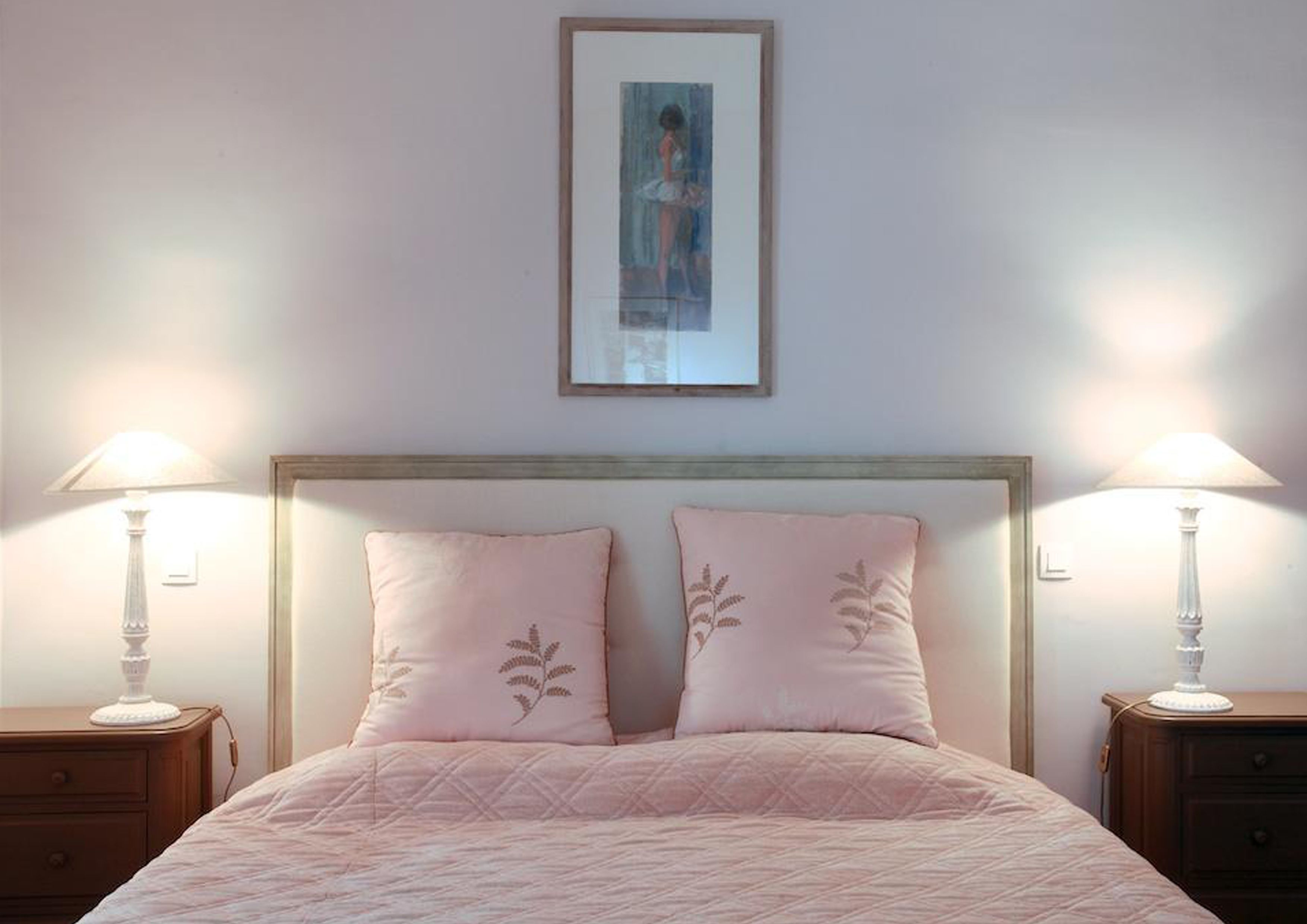 A bedroom with a bed, two nightstands, two lamps, and a framed picture on the wall.
