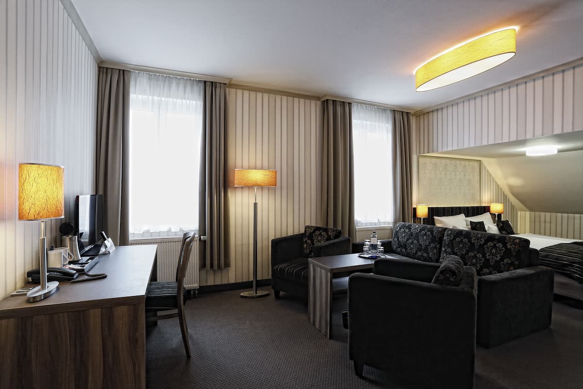 Une chambre d’hôtel équipée d’un bureau, de deux fauteuils, d’un canapé, d’un lampadaire et d’un lit avec une tête de lit.