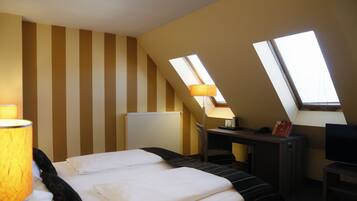 A hotel room with a bed, a desk, a chair, a lamp, and two skylights.