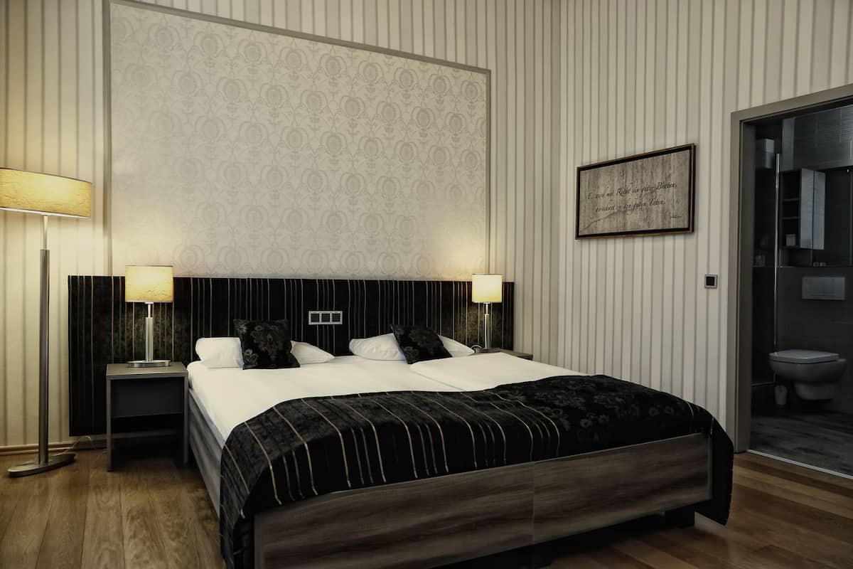 Une chambre à coucher bien aménagée, avec un grand lit, deux tables de chevet avec des lampes, un papier peint à motifs et une citation encadrée accrochée au mur.