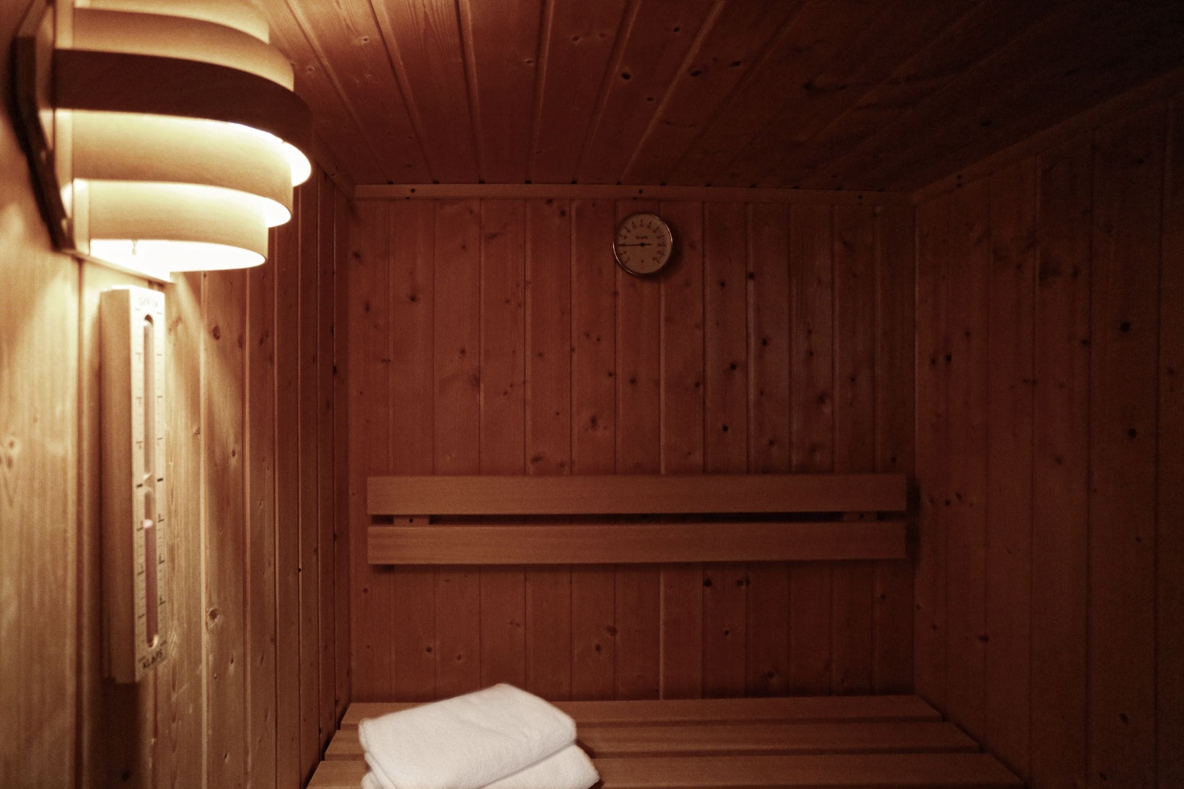 A wooden sauna with benches, a wall-mounted clock, and a towel on the floor.