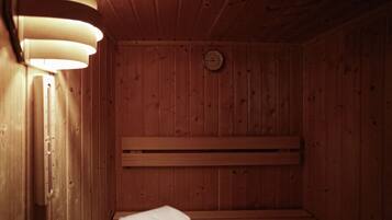 A wooden sauna with benches, a wall-mounted clock, and a towel on the floor.