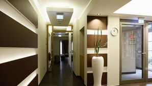 A hotel corridor with a large potted plant, a clock, and a glass door with a sign.