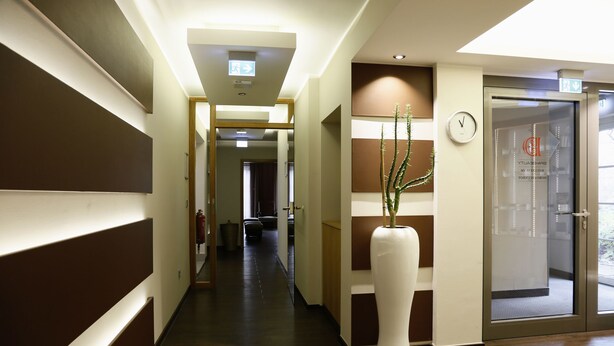 A hotel corridor with a large potted plant, a clock, and a glass door with a sign.