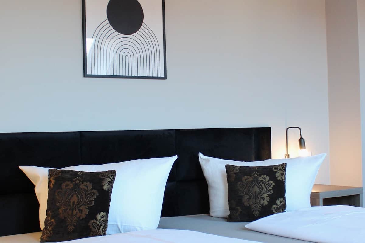 Une chambre d’hôtel avec un grand lit, deux oreillers, une tête de lit et une œuvre d’art accrochée au mur.