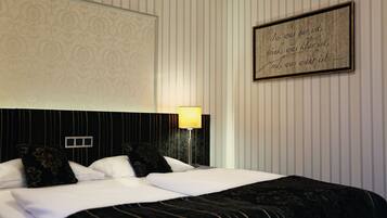 A neatly made bed with white and black linens, a bedside lamp, and a framed quote on the wall.