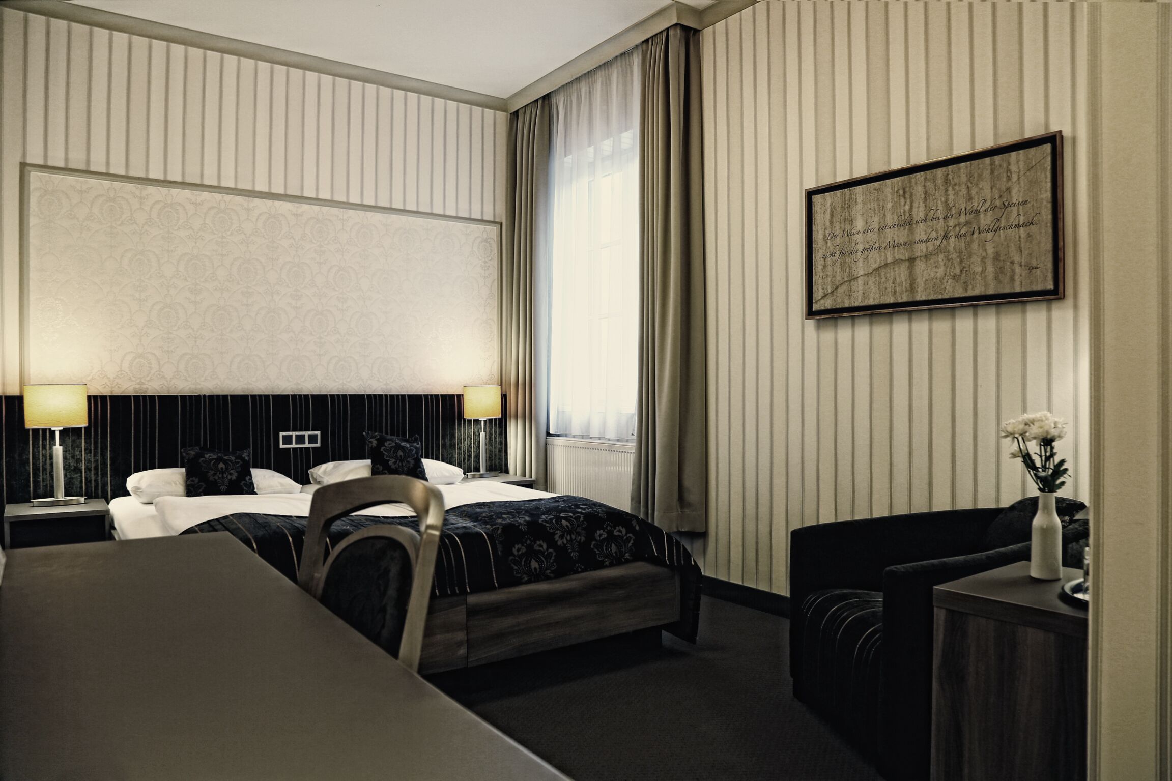 Une chambre d’hôtel avec un grand lit, deux tables de chevet, un bureau, une chaise et un tableau encadré au mur.