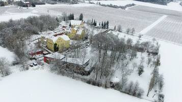 A large, yellow building with multiple windows and a red roof, surrounded by snow-covered fields and trees.