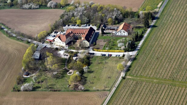 An aerial view of a rural property with multiple buildings, including a large house with a red roof, smaller structures, and a parking area.