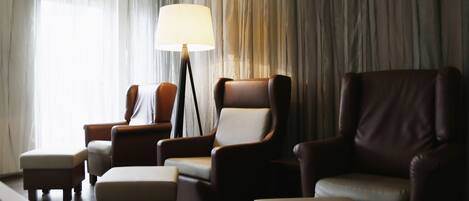A hotel room with a large window, a floor lamp, and several leather armchairs and ottomans.