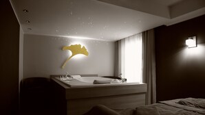 A modern hotel room with a large bed, a bedside table, a mirror, and a wall-mounted light fixture.