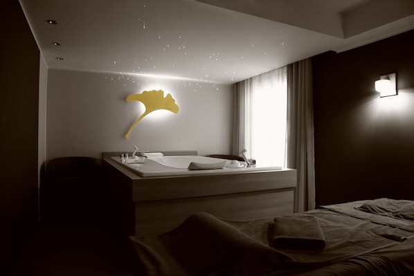 A modern hotel room with a large bed, a bedside table, a mirror, and a wall-mounted light fixture.