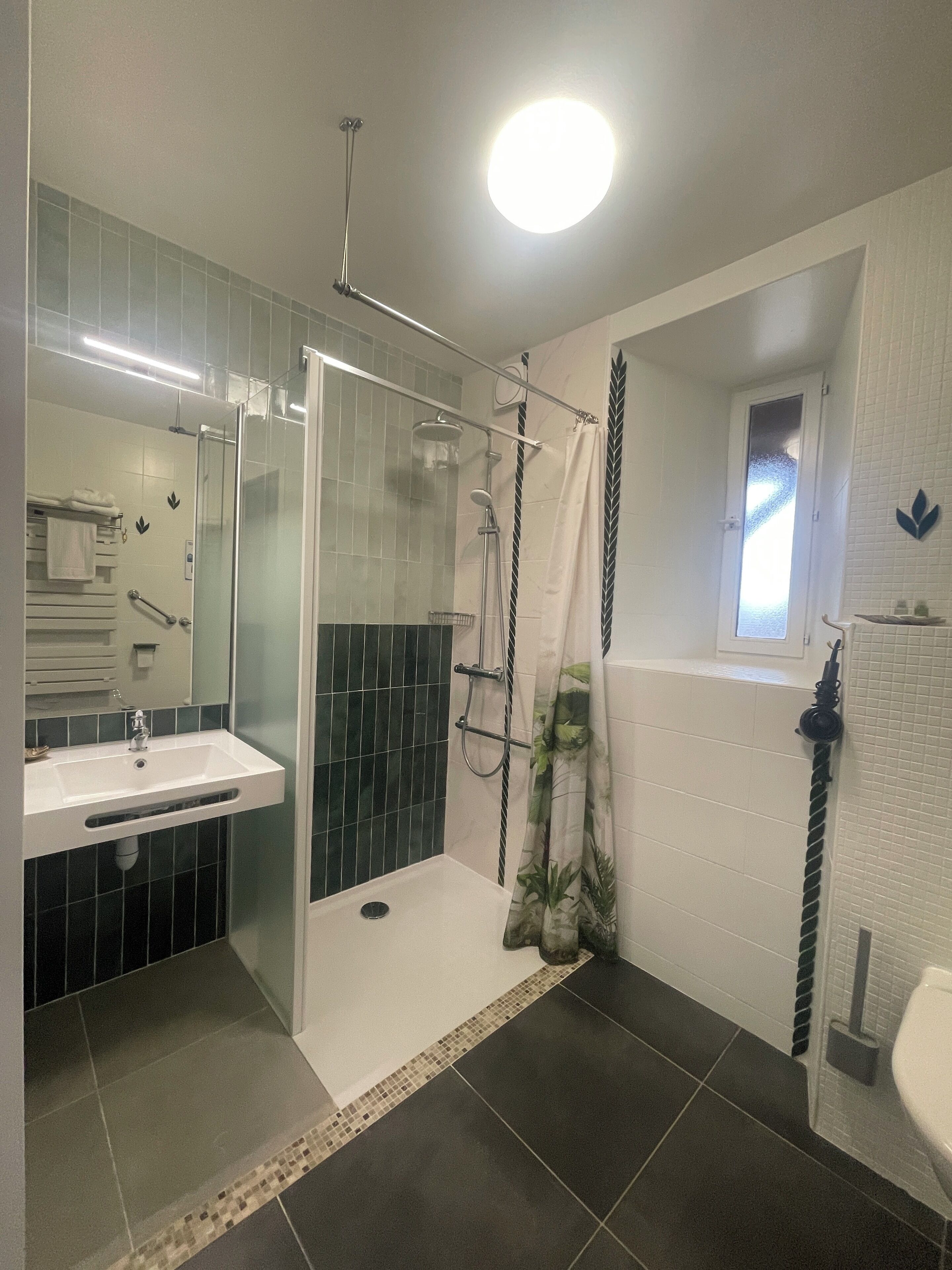 Une salle de bain moderne avec une douche à l’italienne, un lavabo blanc et une petite fenêtre.