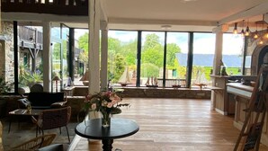 A spacious room with a wooden floor, a round table with chairs, and a view of a balcony with outdoor furniture. - Manoir de Rigourdaine (Plouer-sur-Rance)