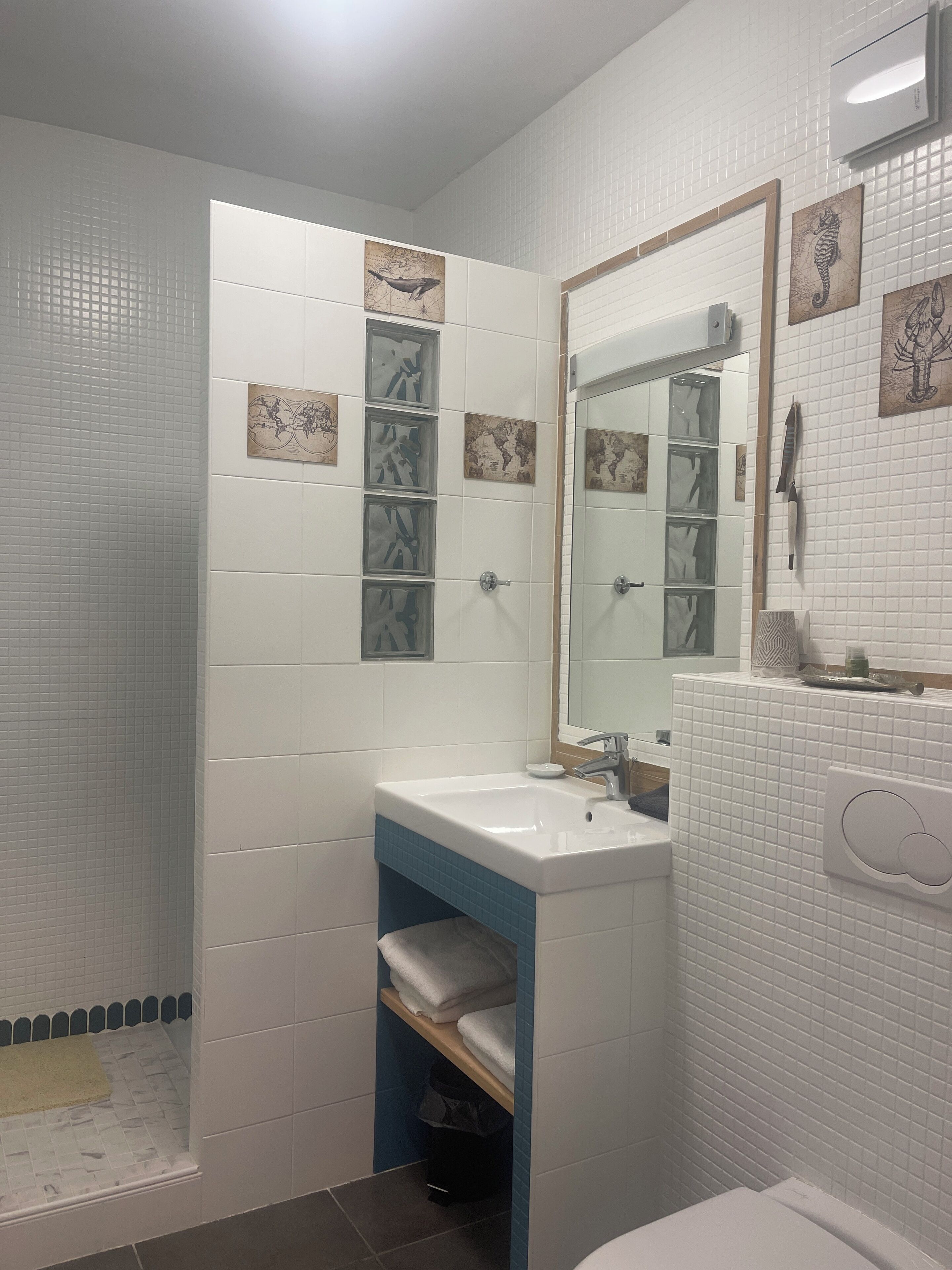 Une salle de bain avec des murs recouverts de carreaux blancs, un lavabo avec un plan de travail bleu, un miroir et un espace douche.