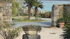 A coastal view with a stone wall, palm trees, and a body of water. - Manoir de Rigourdaine (Plouer-sur-Rance)