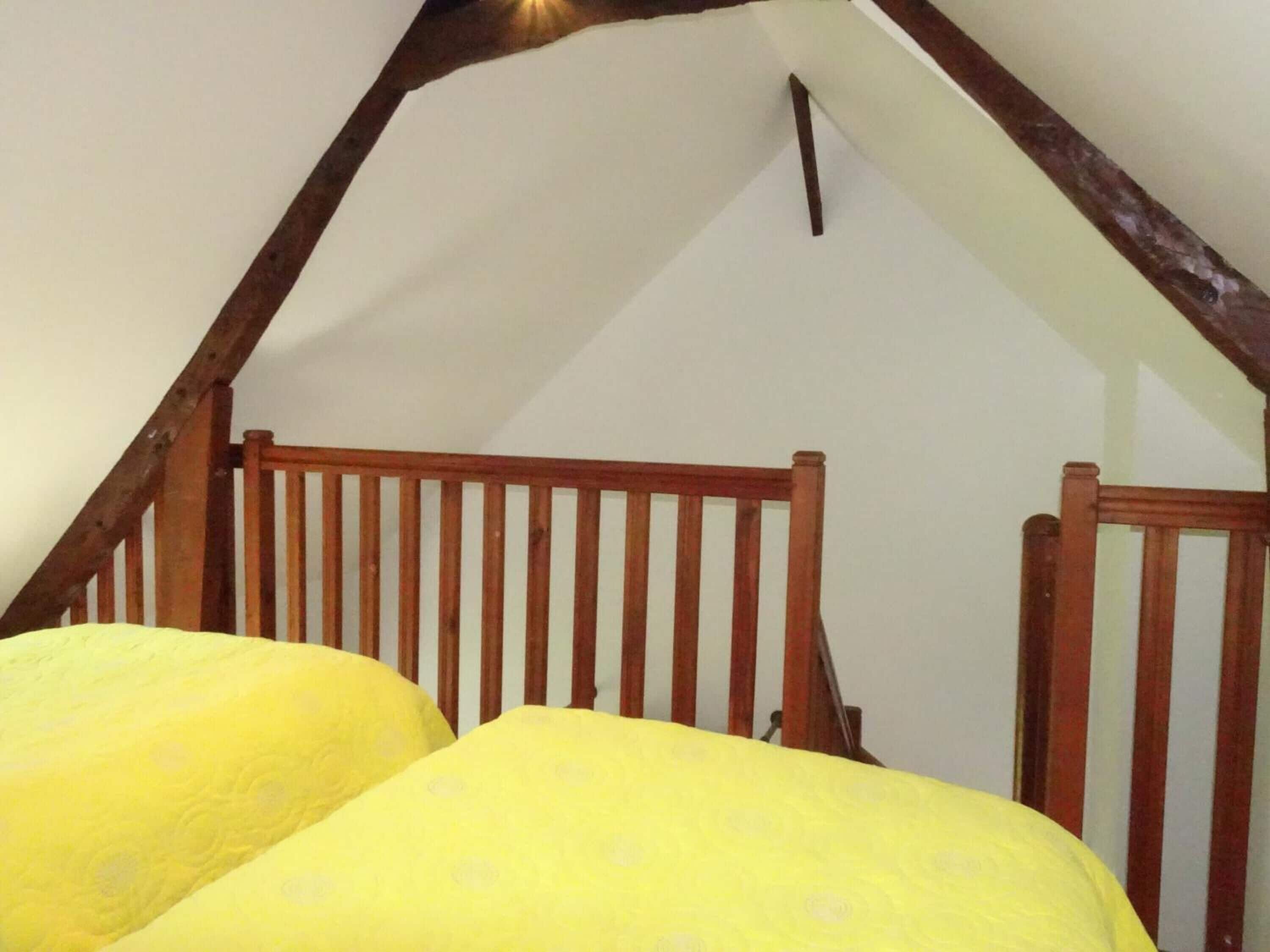 A room with a sloped ceiling and wooden beams, featuring a bed with a yellow patterned bedspread.