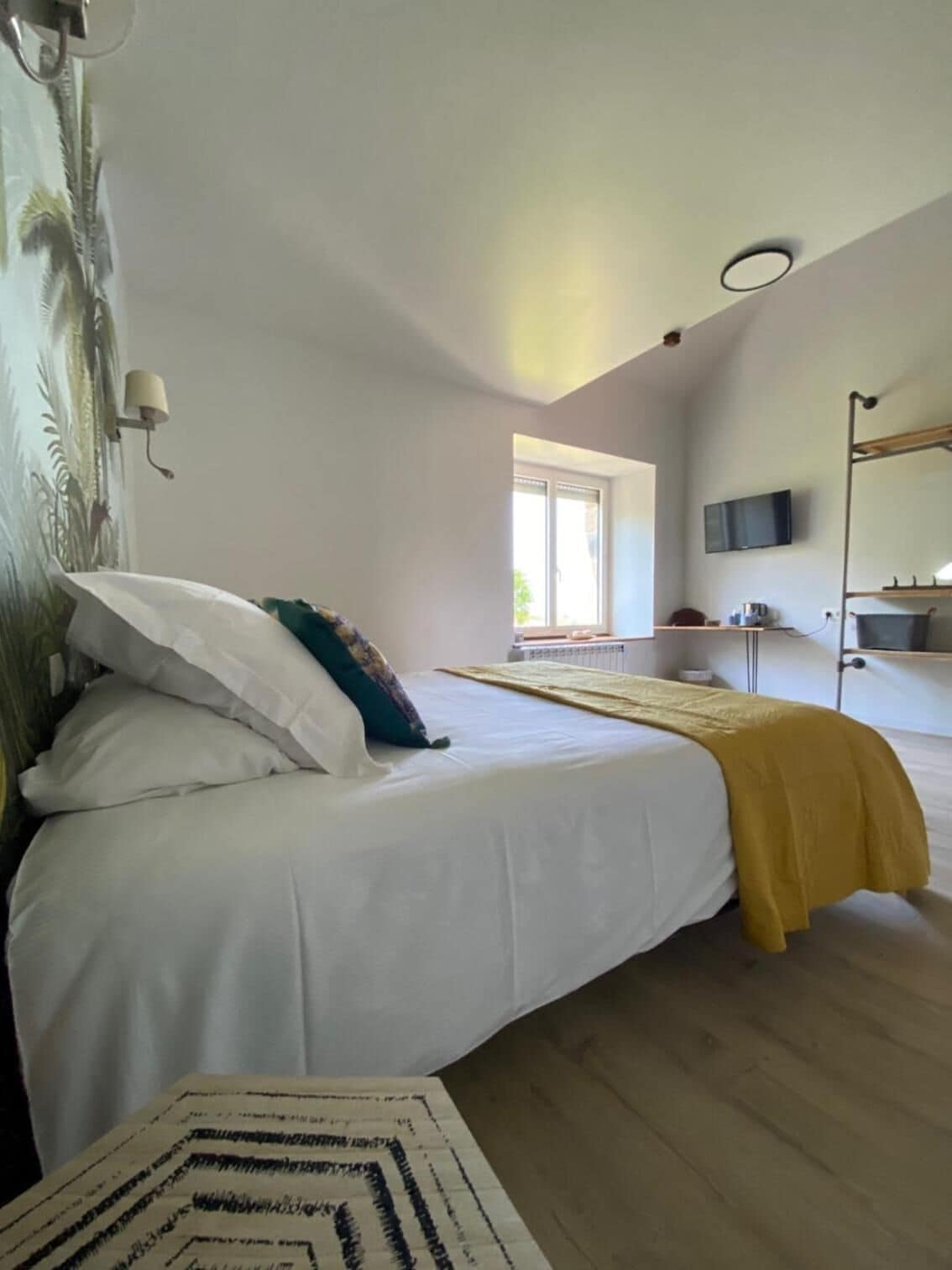 A bedroom with a bed, a window, a TV, and a shelf with items.