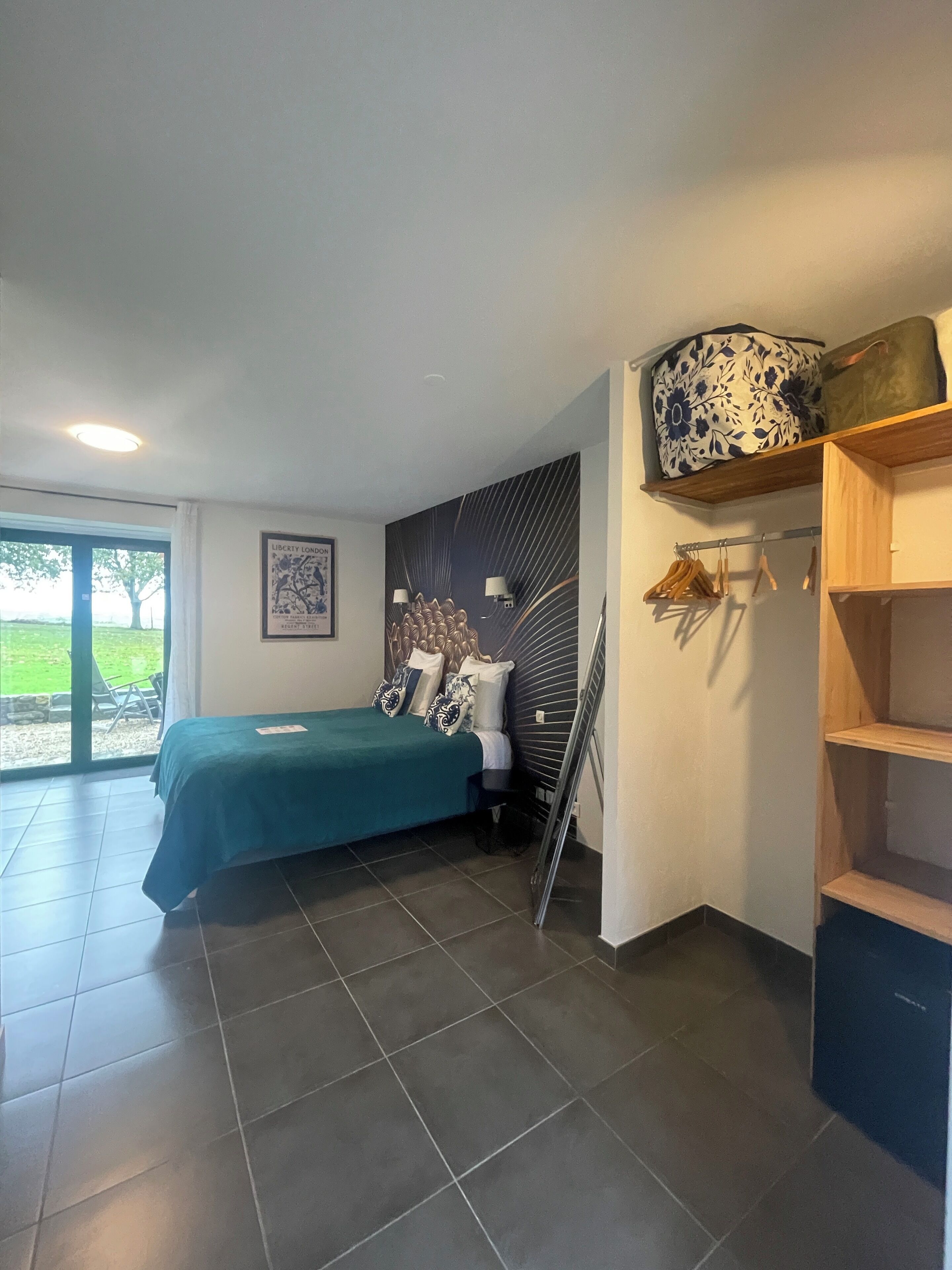 A bedroom with a bed, a wardrobe, a chair, a desk, and a window with a view of greenery.