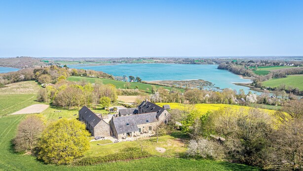 A stone building with a sloped roof, surrounded by green fields and a body of water. - Manoir de Rigourdaine (Plouer-sur-Rance)