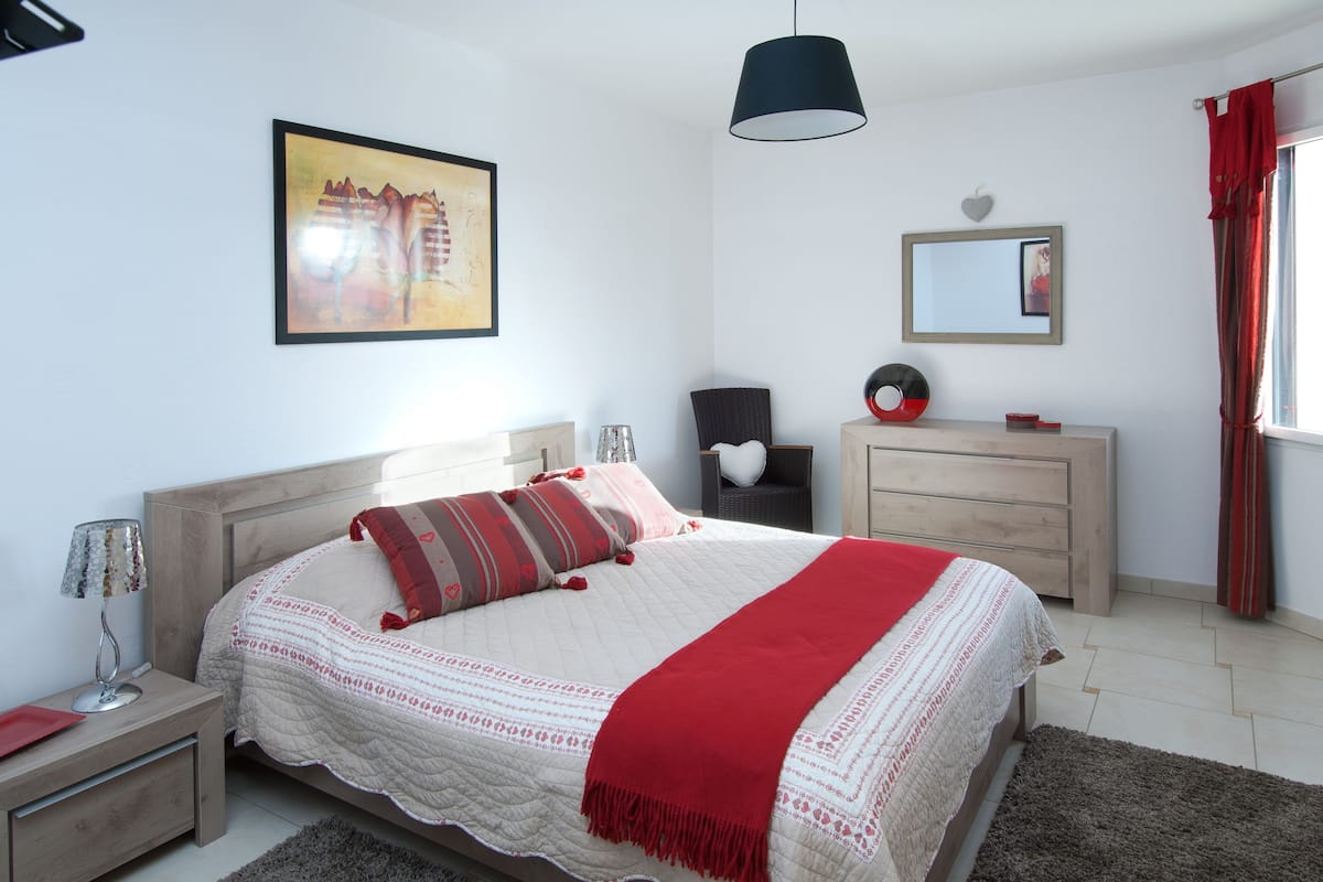 A bedroom with a bed, bedside tables, a dresser, a mirror, and a painting on the wall.