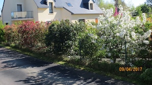 A two-story house with a sloped roof, a balcony on the upper floor, and a garden with flowering bushes. - Aux Portes de Saint-Malo (Saint-Pere)