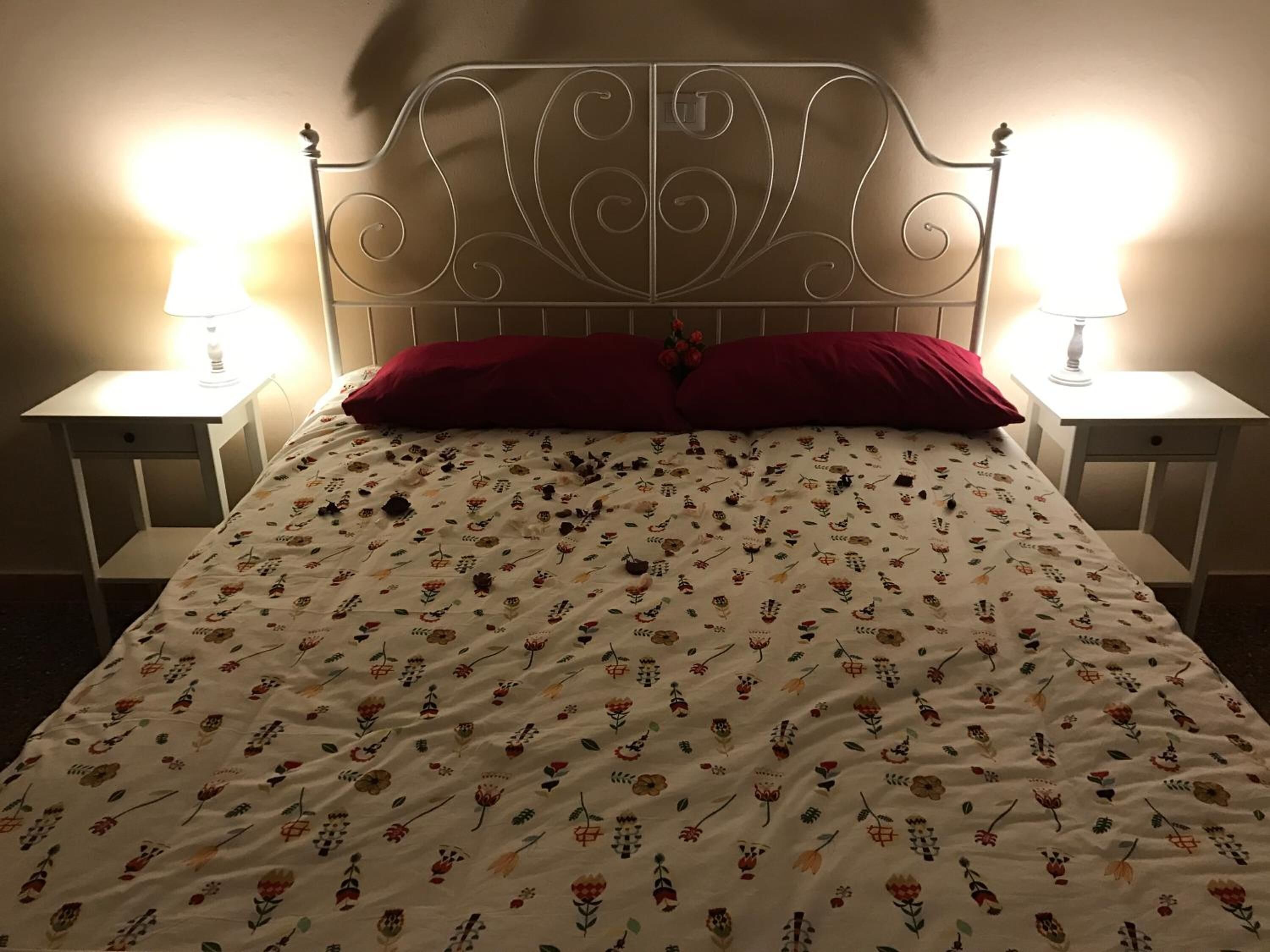 A bed with a floral-patterned duvet, two bedside lamps, and a red pillow.