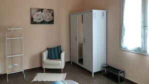 A room with a white wardrobe, a chair with a blue pillow, a white radiator, and a window with a white curtain. - Affittacamere Le Rose (Imola)