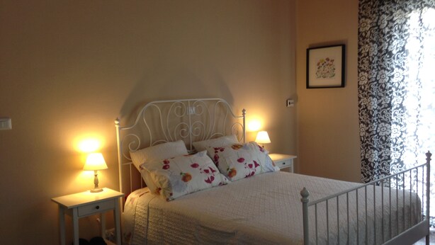 A neatly made bed with floral bedding, two bedside lamps, and a small nightstand with a drawer. - Affittacamere Le Rose (Imola)