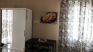 A small room with a kitchenette, a table with two chairs, a painting of roses, and patterned curtains. - Affittacamere Le Rose (Imola)